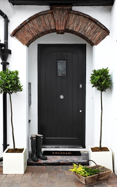 Black door on a white cottage with brick archway 