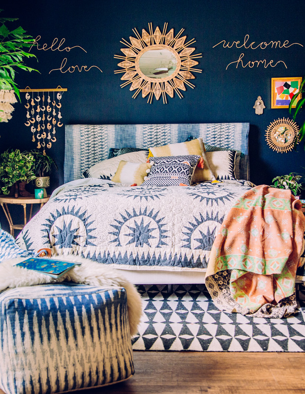 bold boho bedroom. Navy blue wall with gold and green designs. Bedding featuring patterns. 